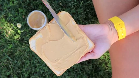 Hand spreading peanut butter on slice of bread for outdoor snack Stock Footage 317221456