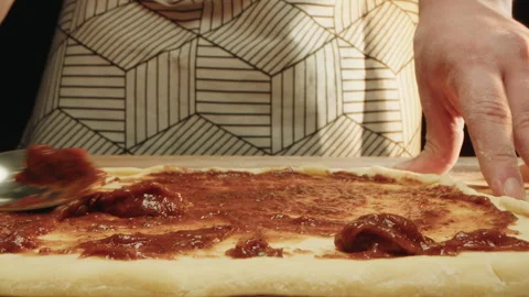 Hand spreading sauce onto dough in rustic kitchen setting 스톡 동영상 331846873
