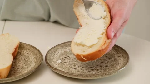 Hand spreading soft cheese on sliced bread over ceramic plate. Breakfast and Stock Footage 307191968