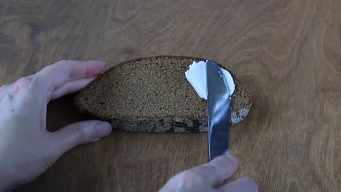 Hand Spreading Soft Cream Cheese on Rye Bread Slice with Knife on Wooden Ta.. Stock Footage 346784729
