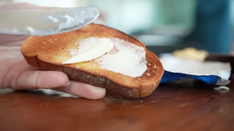 Hand spreads butter on a toasted bread slice with a knife on a wooden table Stock Footage 332245824