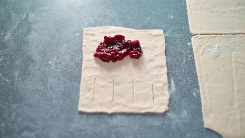 A hand spreads cherry filling onto a sheet of pastry dough placed on a Stock Footage 339095694