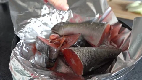Hand sprinkles salt over pieces of red fish wrapped in foil before baking. Stock Footage 336356331