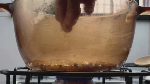 Hand sprinkles white salt while cooking. Hot glass pan with popping popcorn. Stock Footage 148290575