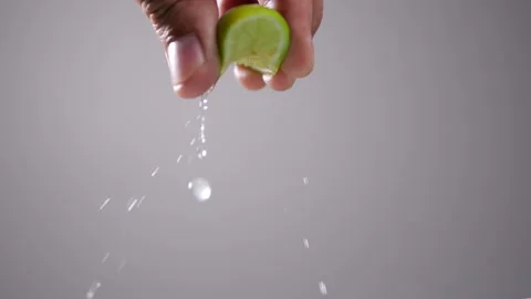 Hand squeeze green lime with lime drop in slow motion on gray background Stock Footage 137989366