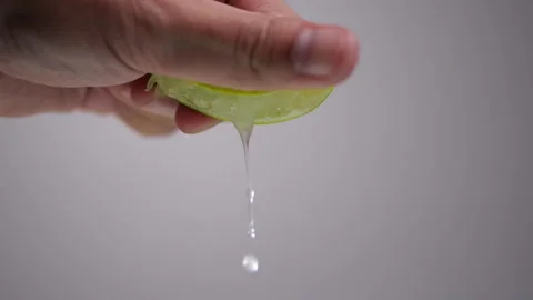 Hand squeeze lime with lime drop in slow motion on gray background Stock Footage