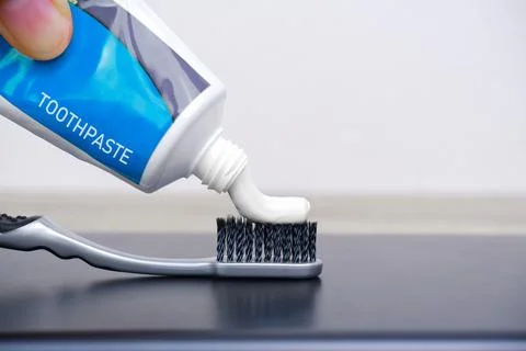 Hand squeezed white toothpaste into a gray toothbrush Stock Photos