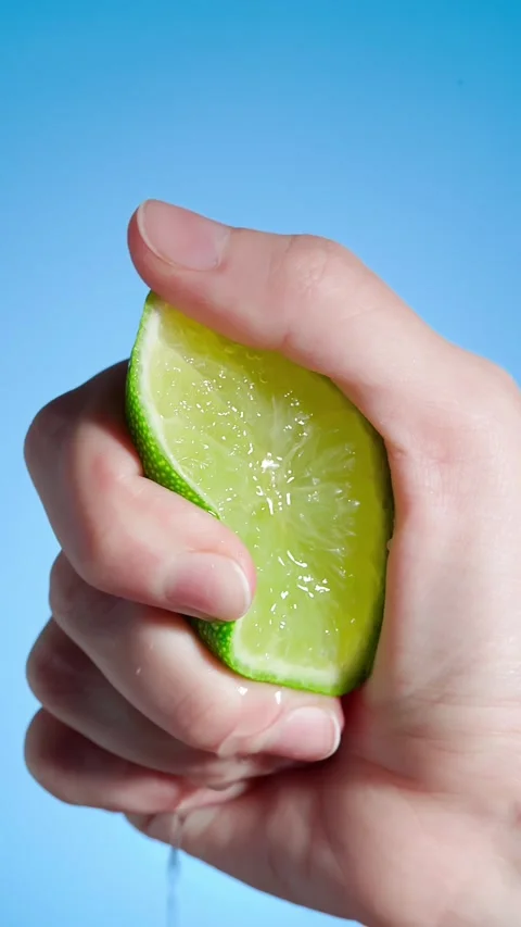 Hand squeezes lime slice and juice flows out Video stock 240311064