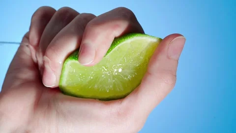 Hand squeezes lime slice and juice flows out Video stock 240315206