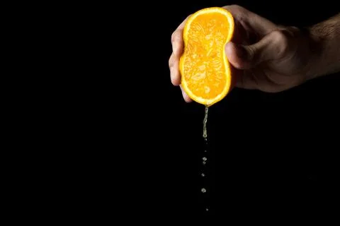 A hand squeezes an orange on a black background.  Stock Photos