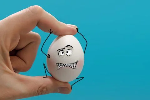 The hand squeezes a white egg in its fingers, which resists, grimacing. On .. Stock Photos