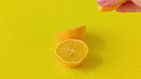 Hand squeezing fresh juice from a lemon half against a solid yellow background. Stock-Footage 338182367
