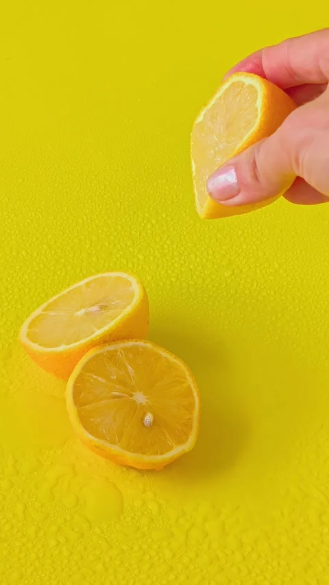 Hand squeezing fresh juice from a lemon half against a solid yellow background. Stock Footage 338182508
