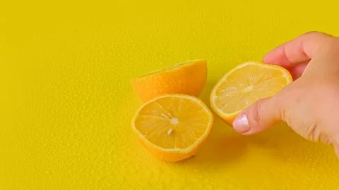 Hand squeezing fresh juice from a lemon half against a solid yellow background. Stock Photos