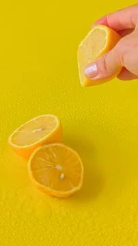 Hand squeezing fresh juice from a lemon half against a solid yellow background. Stock Photos