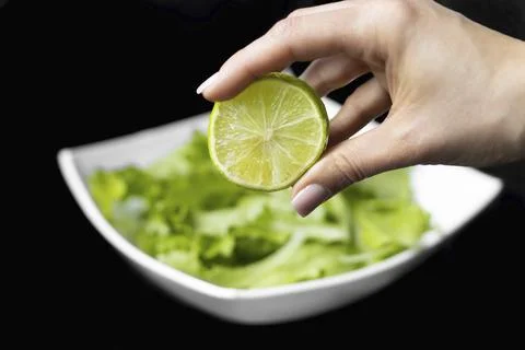 Hand squeezing half of a fresh lime on a black background Stock Photos