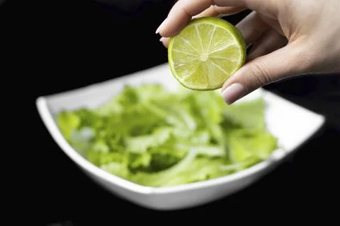 Hand squeezing half of a fresh lime on a black background Stock Photos
