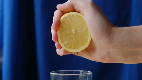 Hand squeezing juice from fresh lemon on a blue background Stock Footage 123167466