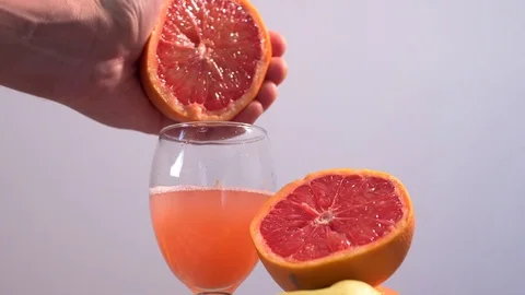 Hand squeezing juice of grapefruit or orange into glass in slow motion 180fps. Stock Footage 83855070
