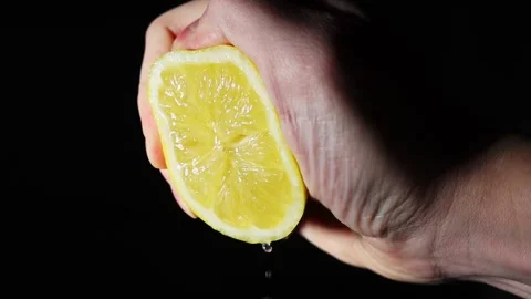 Hand squeezing juice from lemon slowly. freshly squeezed lemon juice on a black Stock Footage 303069891