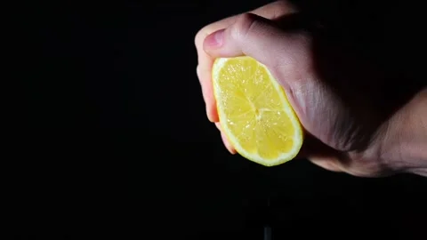 Hand squeezing juice from lemon slowly. freshly squeezed lemon juice on a black Stock Footage 303100712