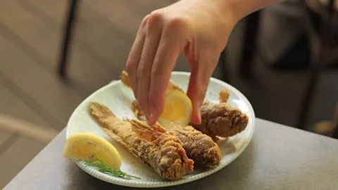 Hand squeezing lemon juice over fried goby fish Stock Footage 344966835