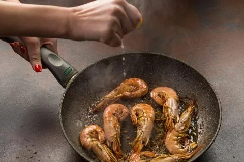 A hand squeezing lemon juice on roasted, grilled shrimp. process of preparati Foto stock