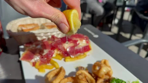 Hand squeezing lemon over fried calamari with serrano ham Stock Footage 333108686