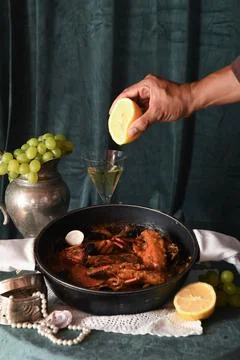 Hand Squeezing Lemon over Seafood Dish on Table with Grapes and Wine Фото