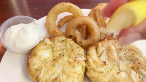 Hand squeezing lemon over two broiled Maryland Crab Cakes 動画素材 344906223