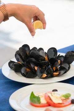 Hand squeezing a lemon slice over some delicious looking boiled mussels on a  Stock Photos