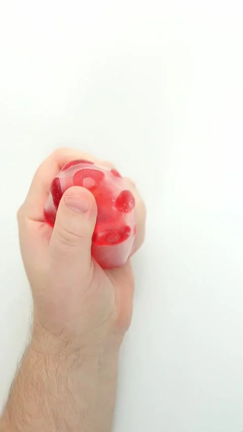 Hand squeezing red gel stress ball with popping bubbles on white Video stock 336265237