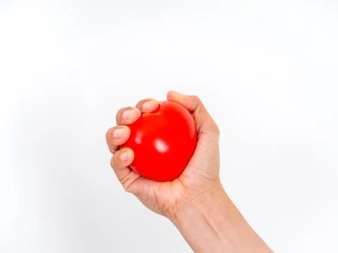Hand squeezing a red heart-shaped stress ball, symbolizing heart health, bl.. Stock Photos
