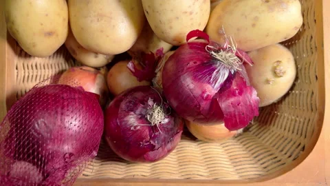 A hand squeezing red onions from a mesh bag into a wicker vegetable basket. Stock Footage 301733434