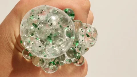 Hand squeezing transparent hydrogel stress ball with green spheres inside Stockbeeldmateriaal 310639491