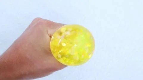 Hand squeezing yellow gel water ball on bright white surface Stockbeeldmateriaal 320099101