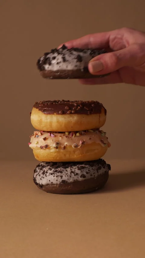 Hand Stacking Glazed Donuts into Tower on Beige Studio Background Stock Footage 331232362