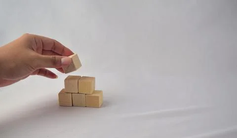 Hand stacking wooden blocks building a pyramid on white background, Constru.. Stock Photos