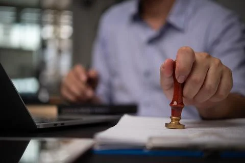 Hand stamping a document in an office setting, symbolizing the process of a.. Stock Photos