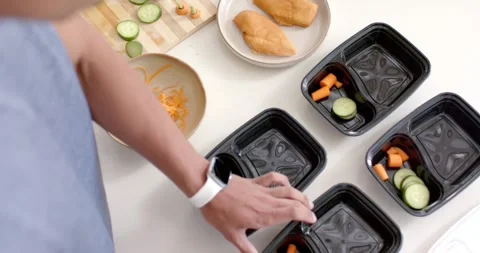 Hand starting meal prep on countertop, slicing cucumber and filling black trays Stock Footage 336175005