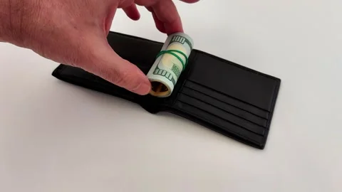 Hand Stashes Rolled-Up 100 Bills into Black Wallet on White Table Video stock 321118391