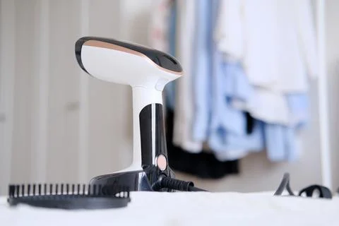 Hand steamer on the background of a rack with clothes in the room Stock Photos