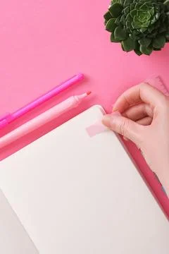 Hand sticks a post-it note in an open notebook with a blank page. Stock Photos