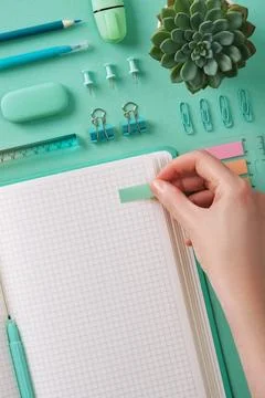 Hand sticks a post-it note in an open notebook with a blank page. Mint green  Stock Photos