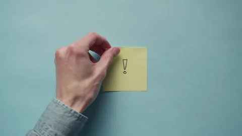 A hand sticks a yellow post it note onto a blue paper backdrop Stock Footage 320557861