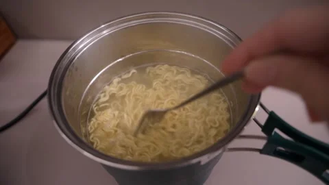 Hand Stirring and Lifting Instant Noodles in Electric Cooking Pot Stock Footage 345498553