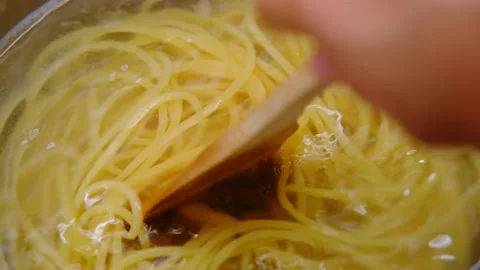 Hand stirring boiled spaghetti pasta in a pot on the stove with a wooden ladle.  Video stock 179287612