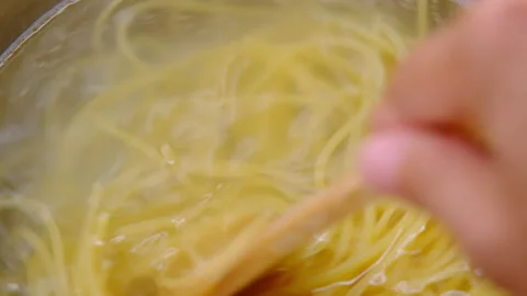 Hand stirring boiled spaghetti pasta in a pot on the stove with a wooden ladle. Vídeo Stock 179294203