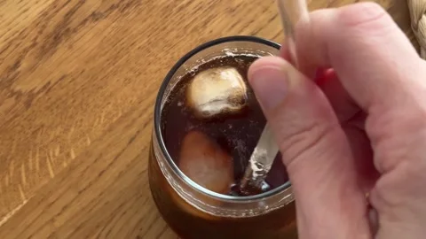 Hand stirring cold iced coffee with a glass straw to espresso in a tall cup Stock Footage 340770996