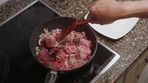 Hand stirring ground meat and onion mixture in black pan with red spatula Stock Footage 323901987